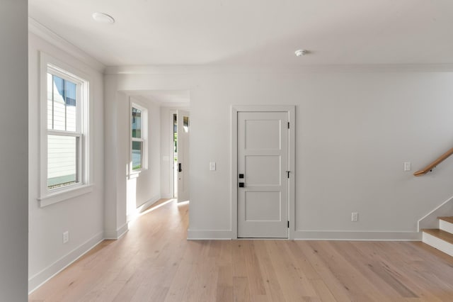 foyer entrance with ornamental molding, baseboards, stairway, and light wood finished floors