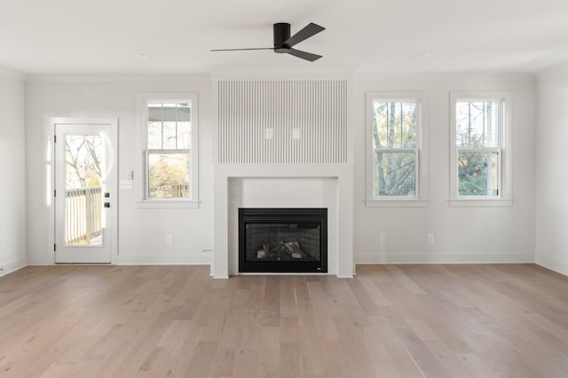 unfurnished living room featuring ornamental molding, a glass covered fireplace, and light wood-style floors