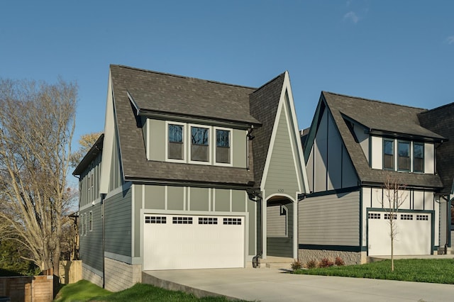 tudor house featuring driveway, a garage, board and batten siding, and roof with shingles