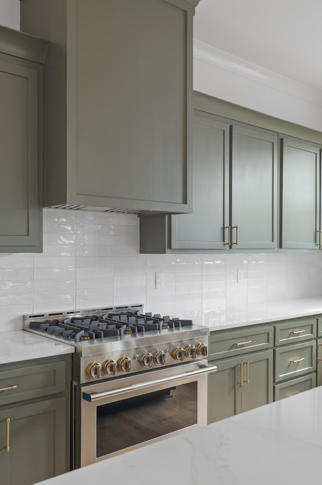 kitchen featuring light stone countertops, backsplash, stainless steel stove, and green cabinetry