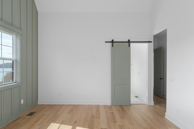 unfurnished room featuring baseboards, visible vents, light wood finished floors, and a barn door