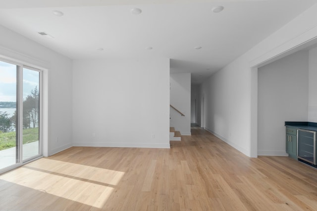 spare room with visible vents, light wood-style floors, beverage cooler, baseboards, and stairs