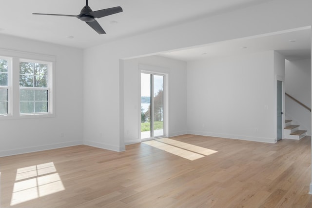 empty room with light wood finished floors, stairway, a ceiling fan, and baseboards