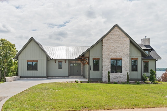 view of front of property featuring metal roof, stone siding, board and batten siding, a chimney, and a front yard