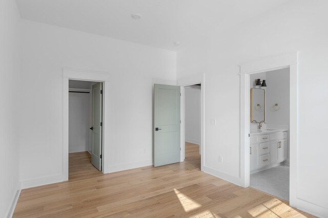 unfurnished bedroom featuring connected bathroom, light wood-style flooring, a sink, baseboards, and a spacious closet