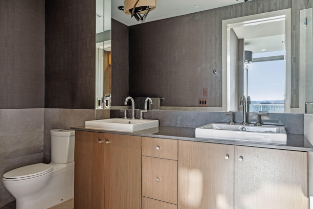 bathroom with toilet, double vanity, tile walls, and a sink