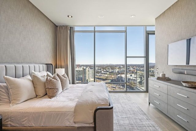 bedroom featuring light wood-style floors, expansive windows, a city view, and wallpapered walls