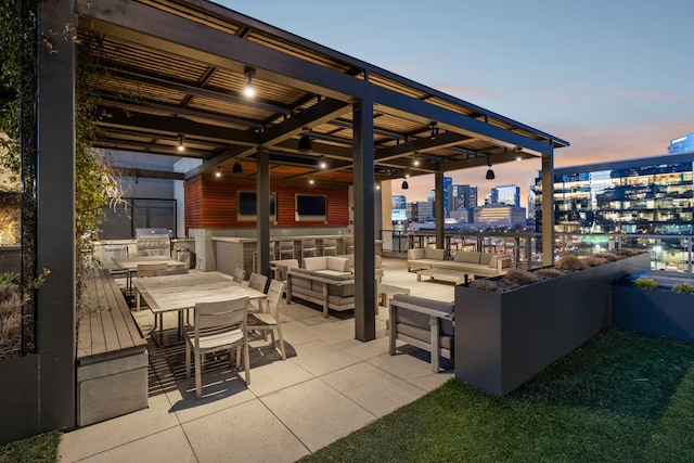 patio terrace at dusk with a city view, outdoor lounge area, an outdoor kitchen, area for grilling, and outdoor dining space