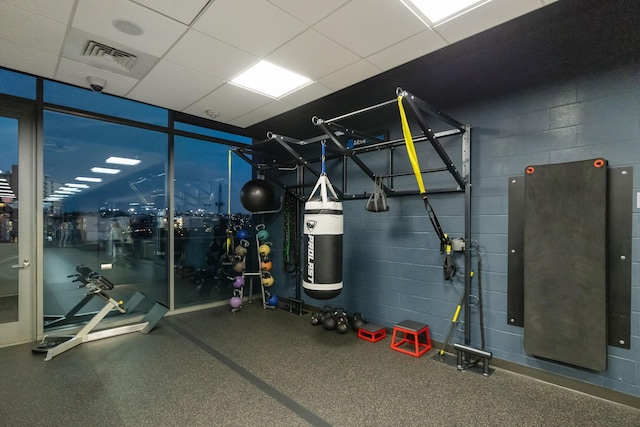 exercise room with a drop ceiling, visible vents, and concrete block wall