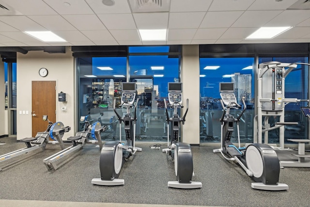 gym with a paneled ceiling, expansive windows, and visible vents