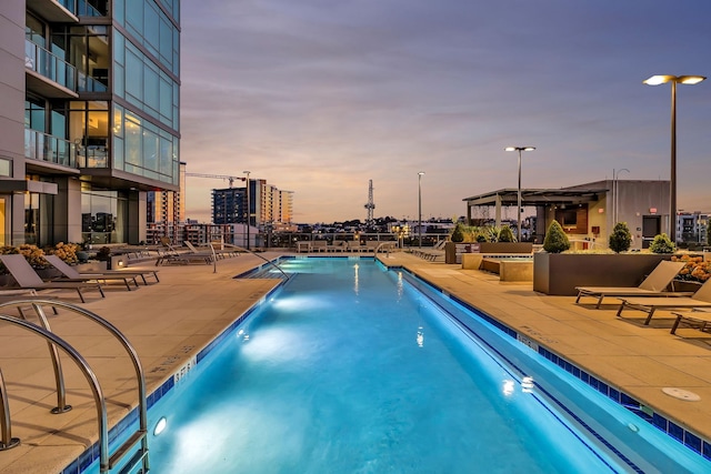 pool at dusk with a patio and a community pool