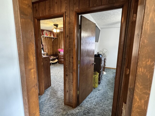 hall with a textured ceiling, wood walls, carpet flooring, and baseboards