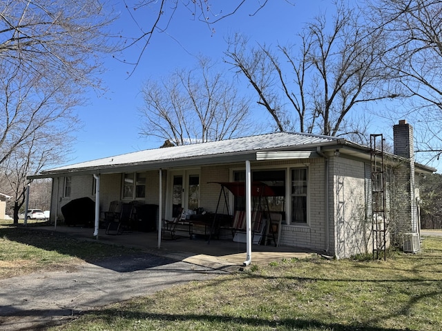 exterior space with metal roof, cooling unit, brick siding, a chimney, and a patio area