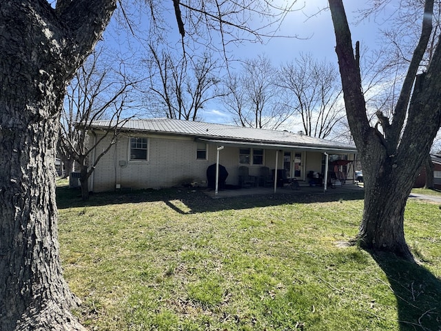 rear view of house featuring metal roof, a yard, brick siding, and a patio