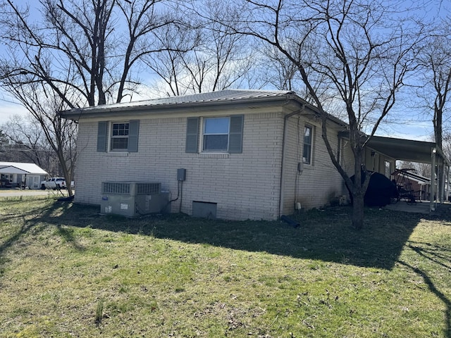 view of side of home featuring metal roof, an attached carport, cooling unit, brick siding, and a lawn