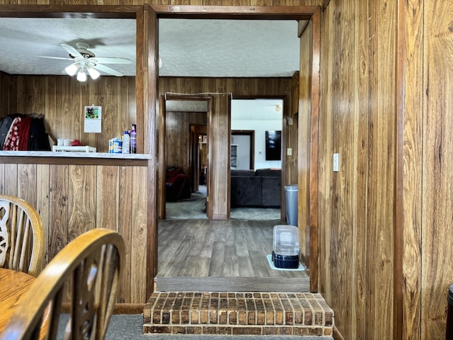 interior space with a textured ceiling, ceiling fan, wood walls, and wood finished floors