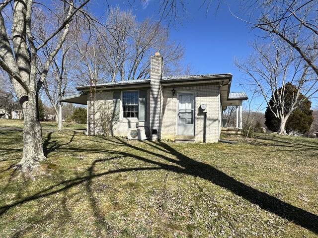 back of house featuring a chimney, a lawn, and brick siding