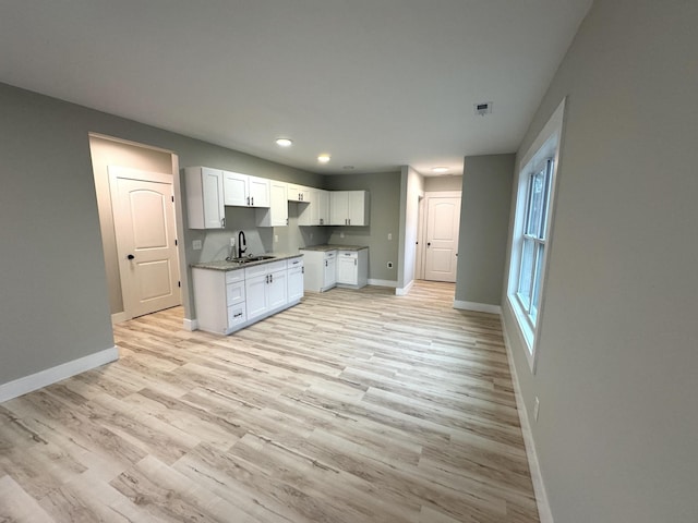 kitchen featuring white cabinets, a sink, light wood-style flooring, and baseboards