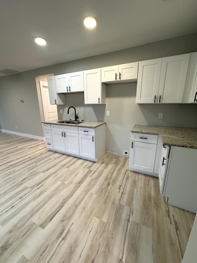 kitchen featuring stone counters, white cabinetry, a sink, light wood-type flooring, and baseboards