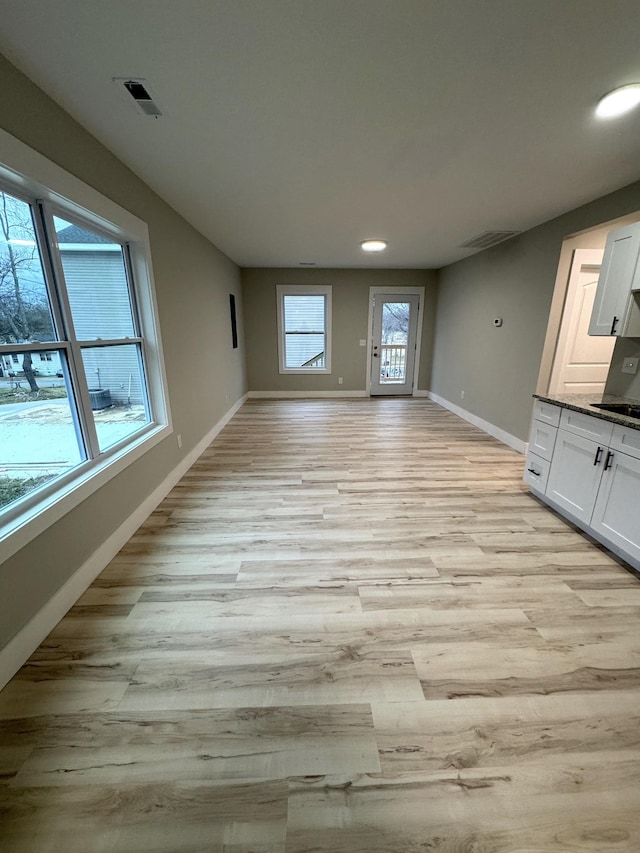 unfurnished living room with visible vents, light wood-style flooring, and baseboards