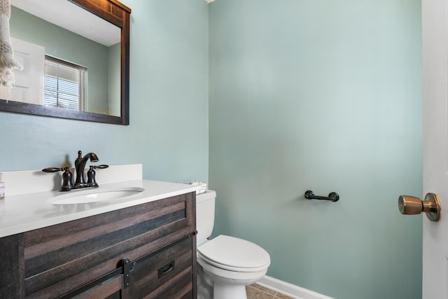 half bath with toilet, tile patterned floors, baseboards, and vanity