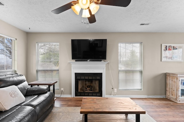 living room with visible vents, a fireplace, baseboards, and wood finished floors