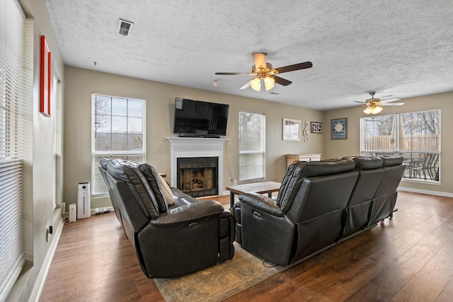 living room with a fireplace, a ceiling fan, visible vents, baseboards, and wood-type flooring