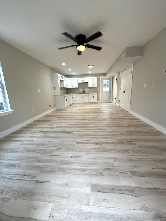 unfurnished living room featuring a sink, visible vents, a ceiling fan, baseboards, and light wood finished floors