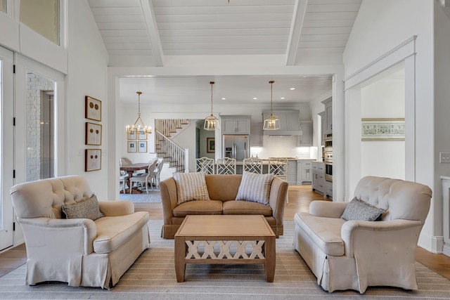 living room featuring vaulted ceiling with beams, light wood-style floors, stairs, and a notable chandelier