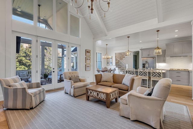 living area with french doors, light wood finished floors, stairway, a chandelier, and beamed ceiling