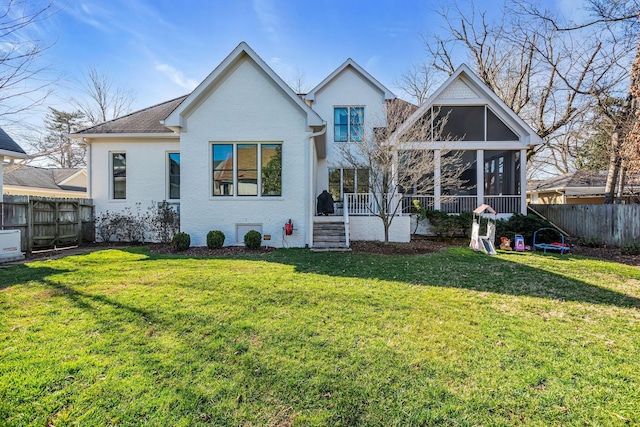 rear view of house with a lawn, fence, and a sunroom