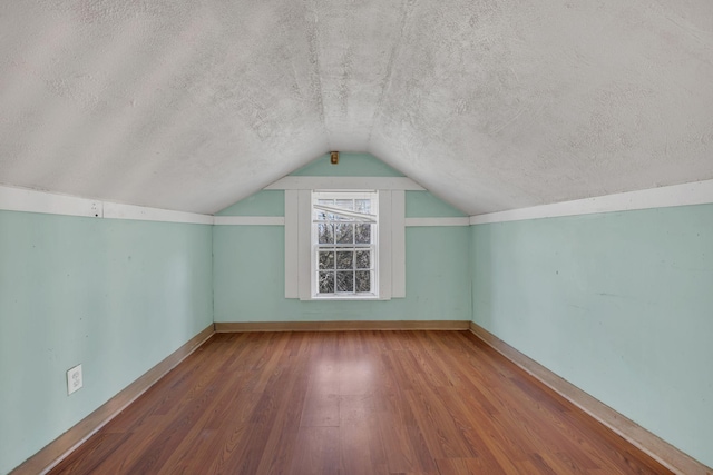 additional living space with lofted ceiling, a textured ceiling, wood finished floors, and baseboards