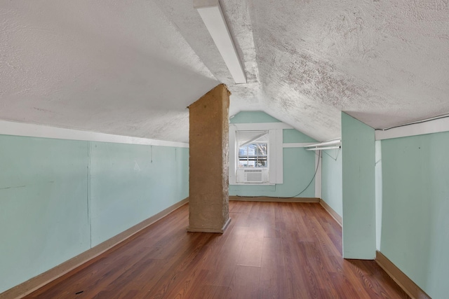 additional living space with a textured ceiling, baseboards, vaulted ceiling, and wood finished floors