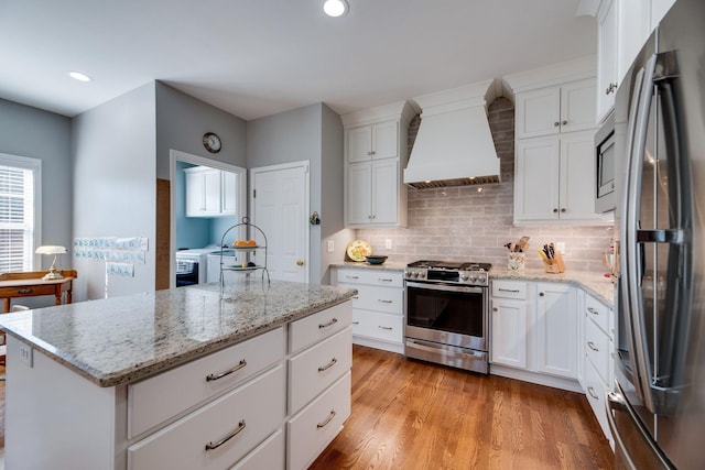 kitchen featuring washer and clothes dryer, stainless steel appliances, tasteful backsplash, custom range hood, and light wood-type flooring