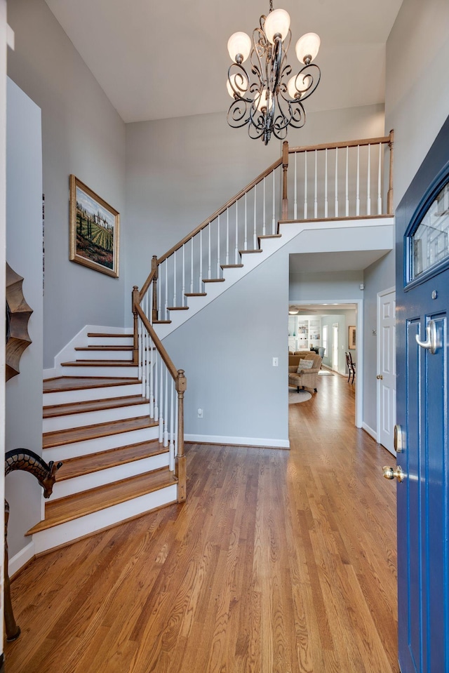 foyer entrance featuring a chandelier, stairway, wood finished floors, and baseboards