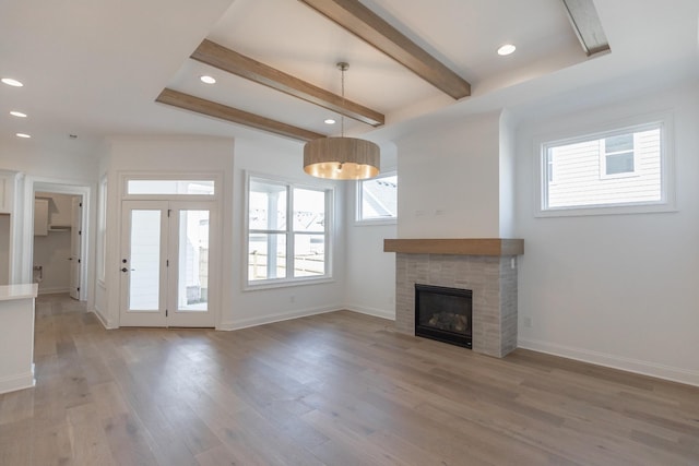 unfurnished living room featuring light wood-type flooring, beam ceiling, a healthy amount of sunlight, and baseboards