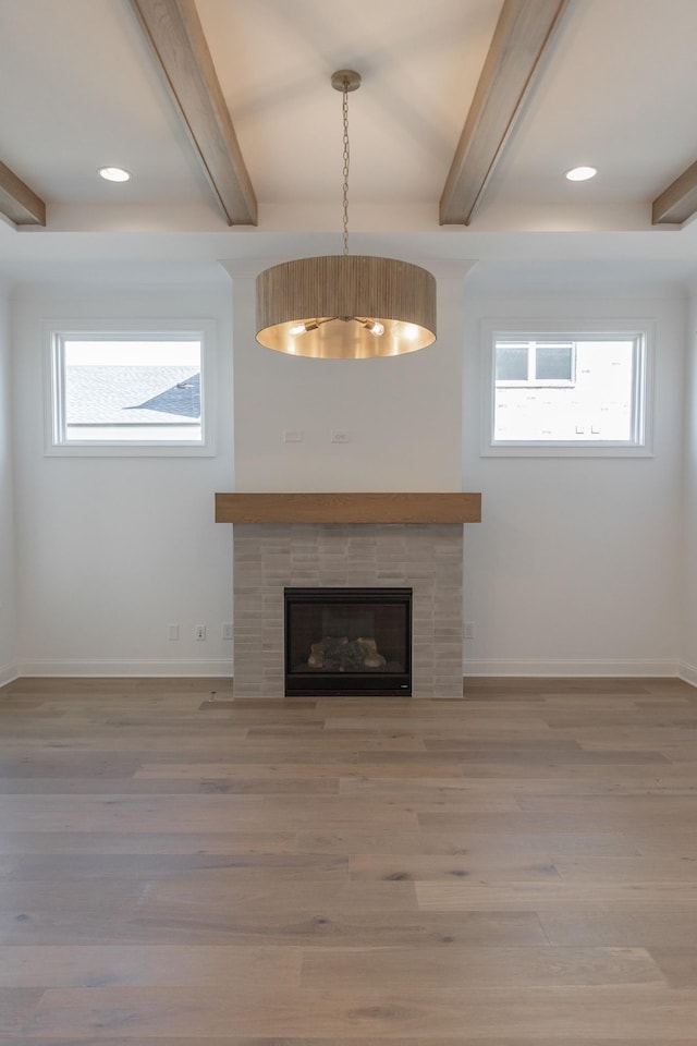 unfurnished living room featuring a healthy amount of sunlight, a fireplace, wood finished floors, and beamed ceiling