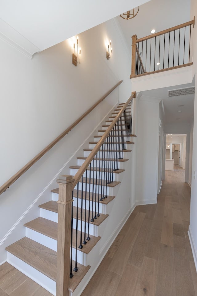 stairway with ornamental molding, baseboards, a high ceiling, and wood finished floors