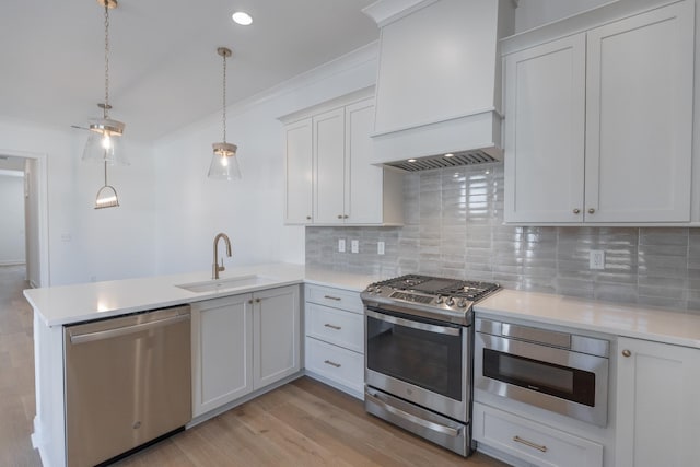 kitchen with appliances with stainless steel finishes, a peninsula, light countertops, premium range hood, and a sink