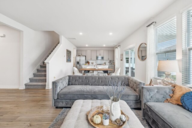 living area with recessed lighting, visible vents, baseboards, stairs, and light wood finished floors