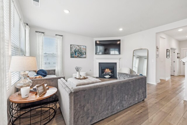 living room with a warm lit fireplace, arched walkways, recessed lighting, wood finished floors, and visible vents