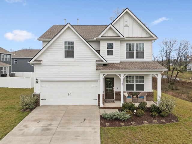 traditional-style home with driveway, covered porch, fence, a front lawn, and board and batten siding