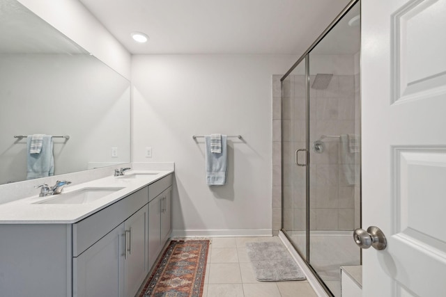 bathroom featuring double vanity, baseboards, tile patterned flooring, a shower stall, and a sink