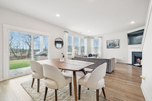 dining area with baseboards, a fireplace with flush hearth, light wood-style flooring, and recessed lighting