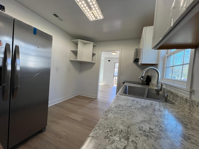 kitchen with visible vents, a sink, white cabinets, light wood-style floors, and stainless steel refrigerator with ice dispenser