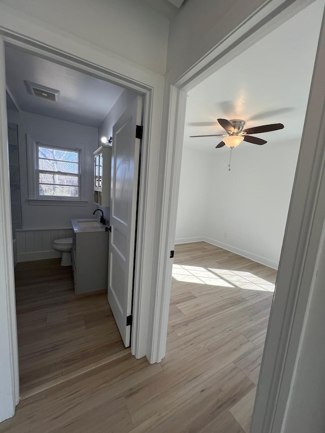 hall featuring a sink, light wood-type flooring, baseboards, and visible vents