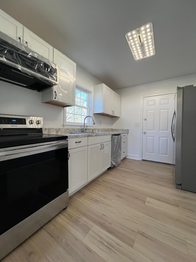 kitchen with a sink, light wood-style floors, appliances with stainless steel finishes, exhaust hood, and white cabinets