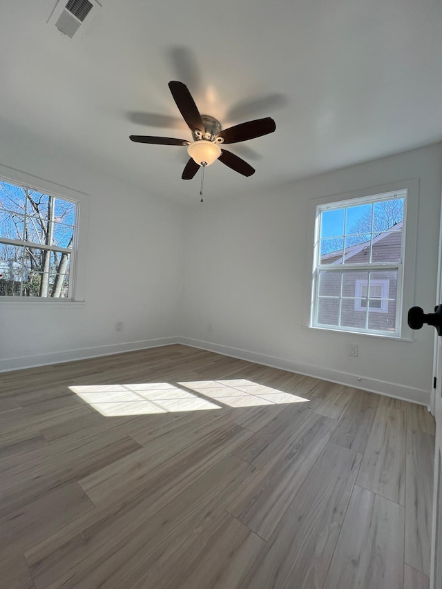 empty room featuring a wealth of natural light, visible vents, light wood-type flooring, and baseboards