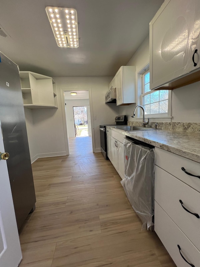 kitchen with light wood finished floors, a sink, stainless steel appliances, white cabinetry, and open shelves