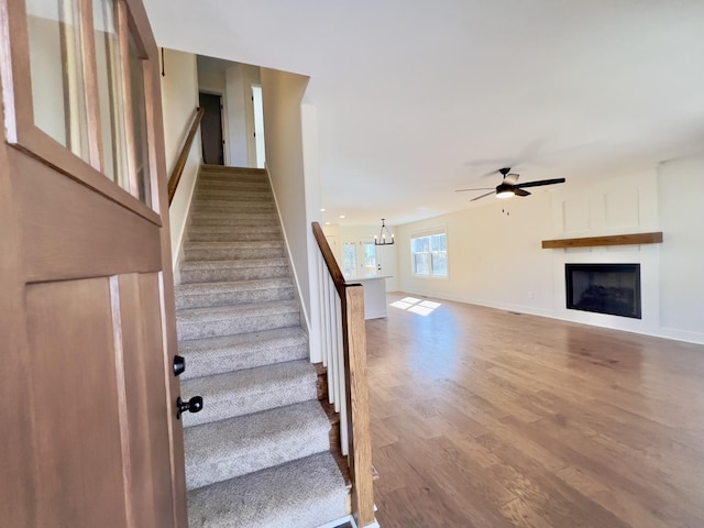 staircase featuring ceiling fan with notable chandelier, a fireplace, baseboards, and wood finished floors